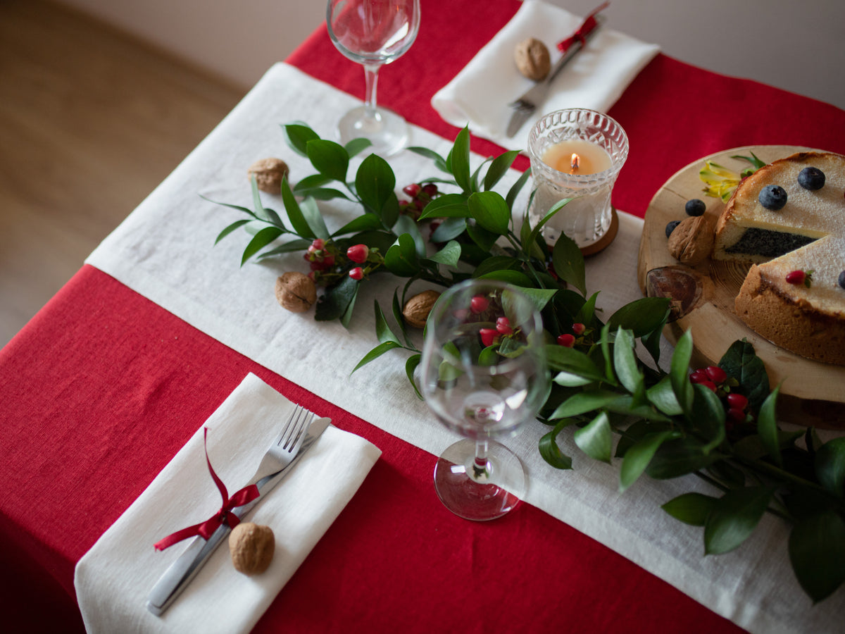 Decorative table setting with red linen tablecloth, greenery, candles, and a cake.