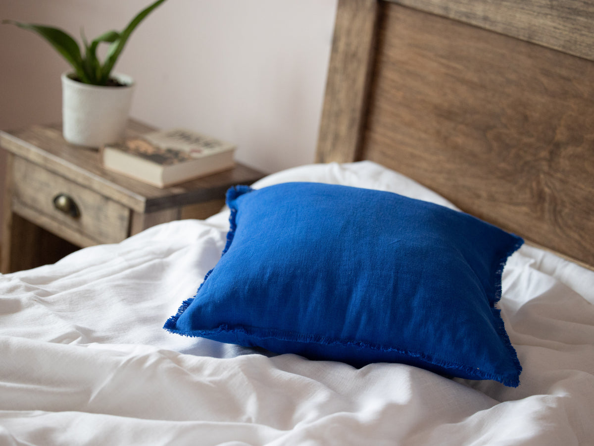 Blue pillow on a bed with a wooden headboard and side table in the background.