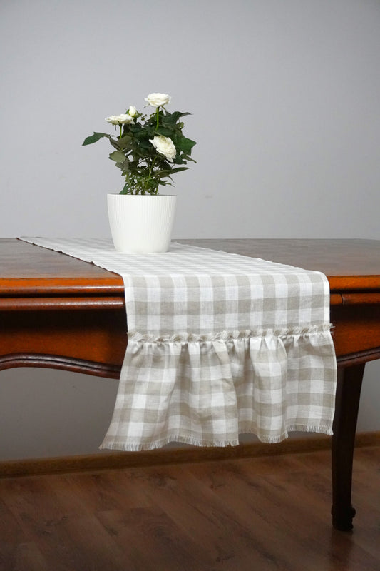 Table with a checkered table runner, white flowers in a vase, and a plain background