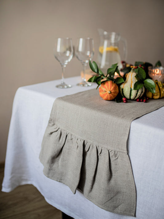 Table setting with a not dyed linen ruffled table runner, wine glasses, and decorative pumpkins.