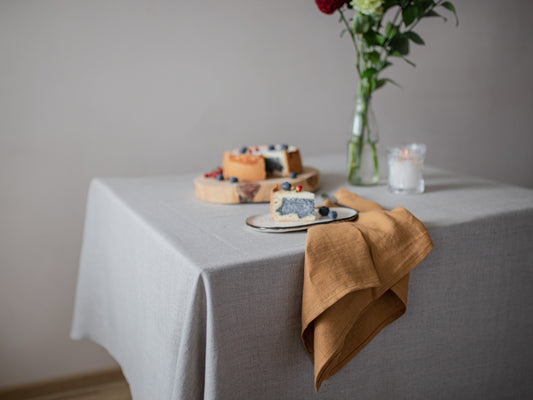 Table setting with a gray tablecloth, brown napkin, and small cake on a white surface.