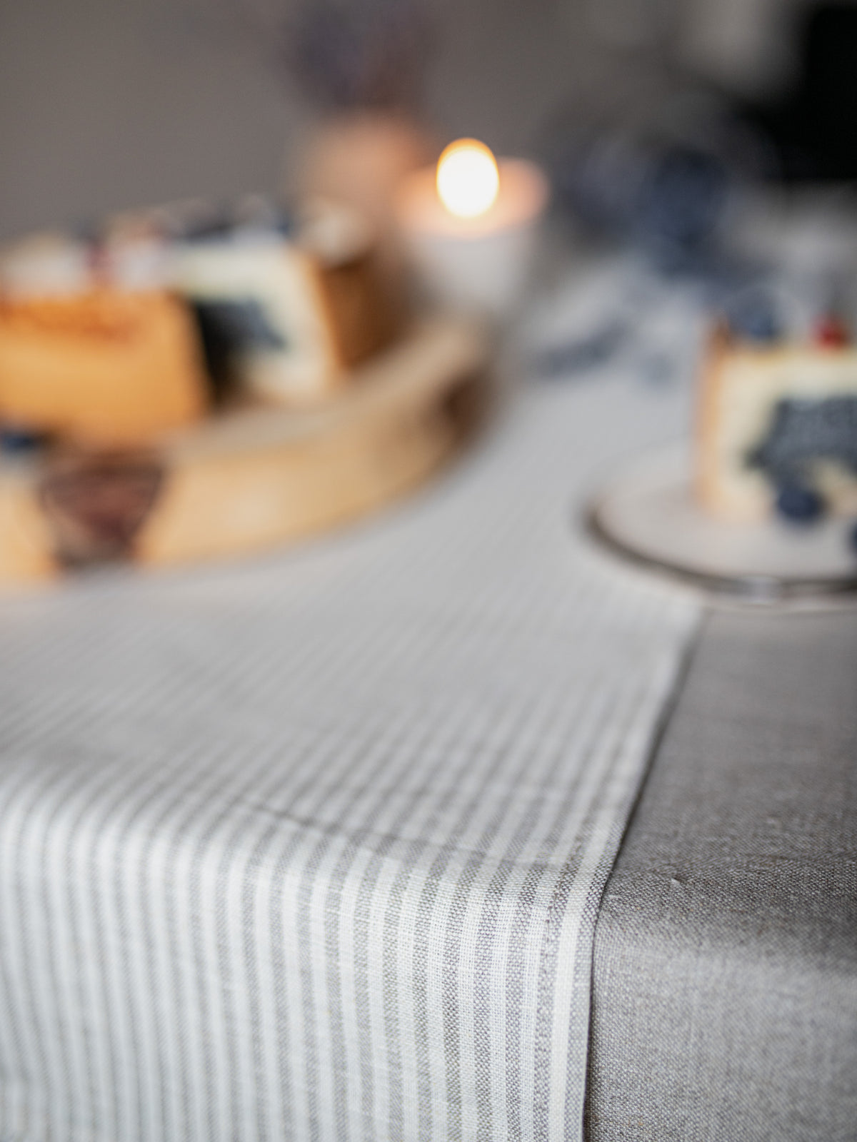 a light gray and white striped table runner laid across a table, with a gray tablecloth.