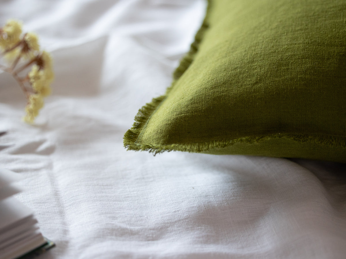 Close-up of a sage green fabric pillow on a white surface