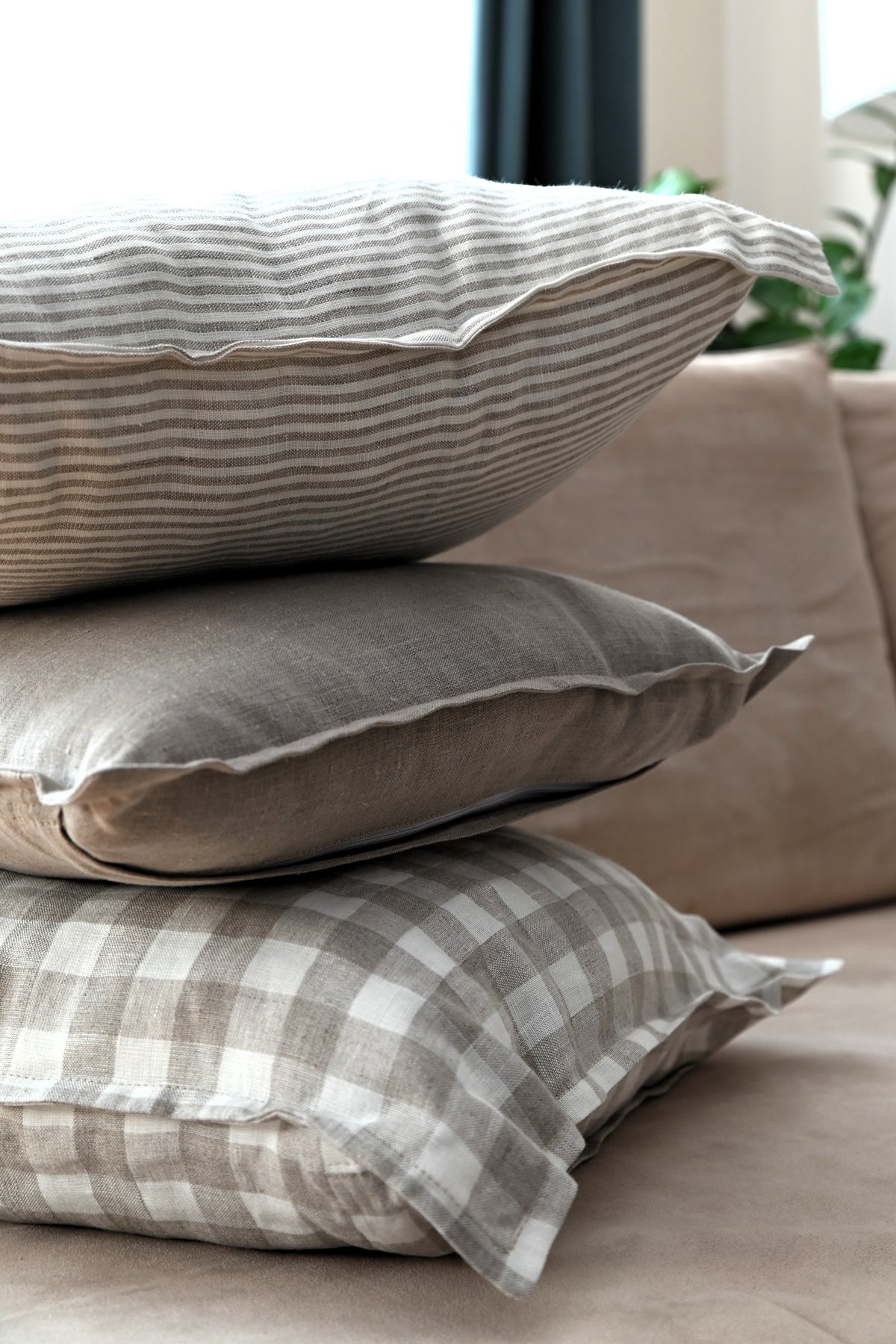 Stack of decorative linen pillows with striped, solid, and checkered patterns on a sofa.