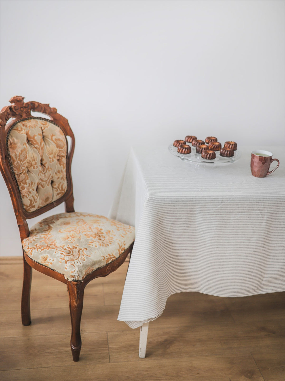 Vintage chair next to a table with a striped linen tablecloth, glass of water, and small plate of cookies.