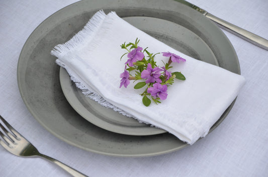 White fringed napkin with purple flowers on a stack of plates with cutlery
