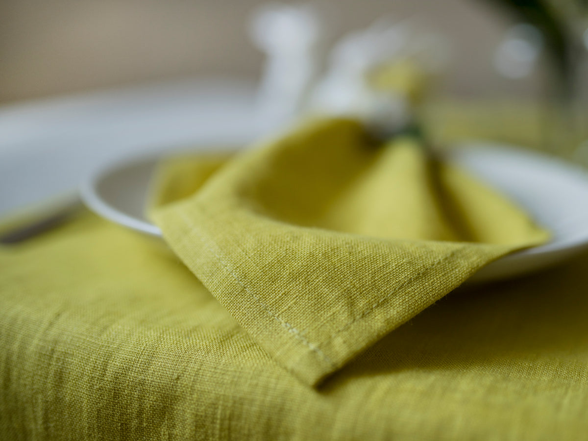chartreuse linen napkin folded on a white plate with a blurred background