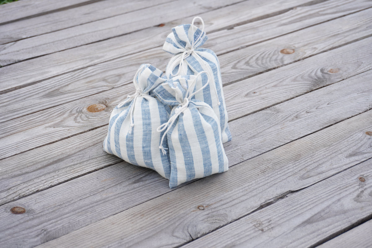 Three small pouches in a light blue and white striped linen fabric, arranged on a weathered gray wooden deck.
