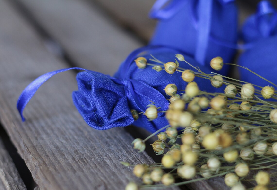 A close-up of blue  linen fabric pouches tied with blue ribbon, arranged on a rustic wooden surface with dried baby's breath flowers in the foreground.