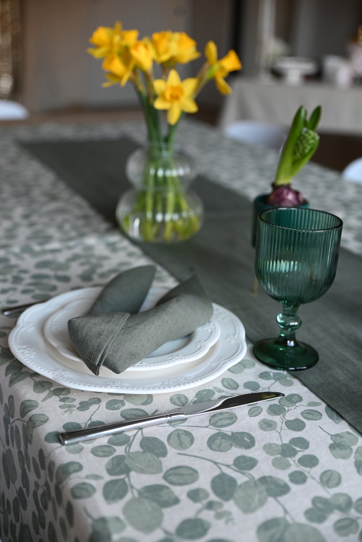 Close-up of a table setting with a green glass, napkin, and flowers on a patterned tablecloth.