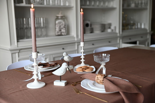 Dining table setting with candles, plates, cacao brown linen napkins and decorative birds in a room.