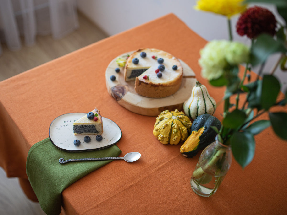 Table setting with a pie, small plate of dessert, and decorative pumpkins on a burnt orange linen 
tablecloth.