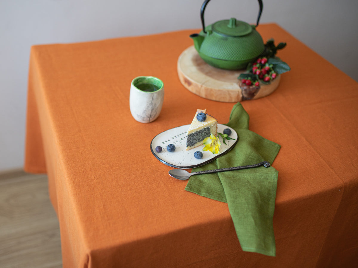 Tea set with a green teapot, cup, and cake on an burnt orange tablecloth.