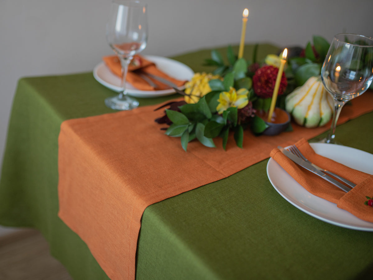 Set table with green and orange tablecloth, candles, and decorative items.