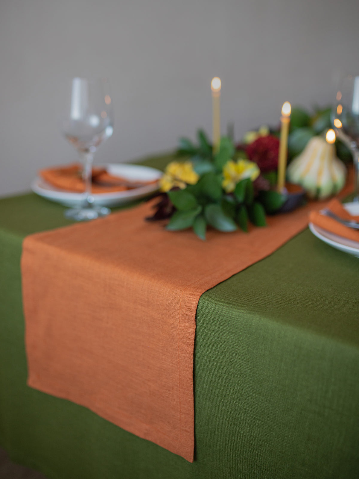 Table setting with an orange runner, green tablecloth, and floral centerpiece.