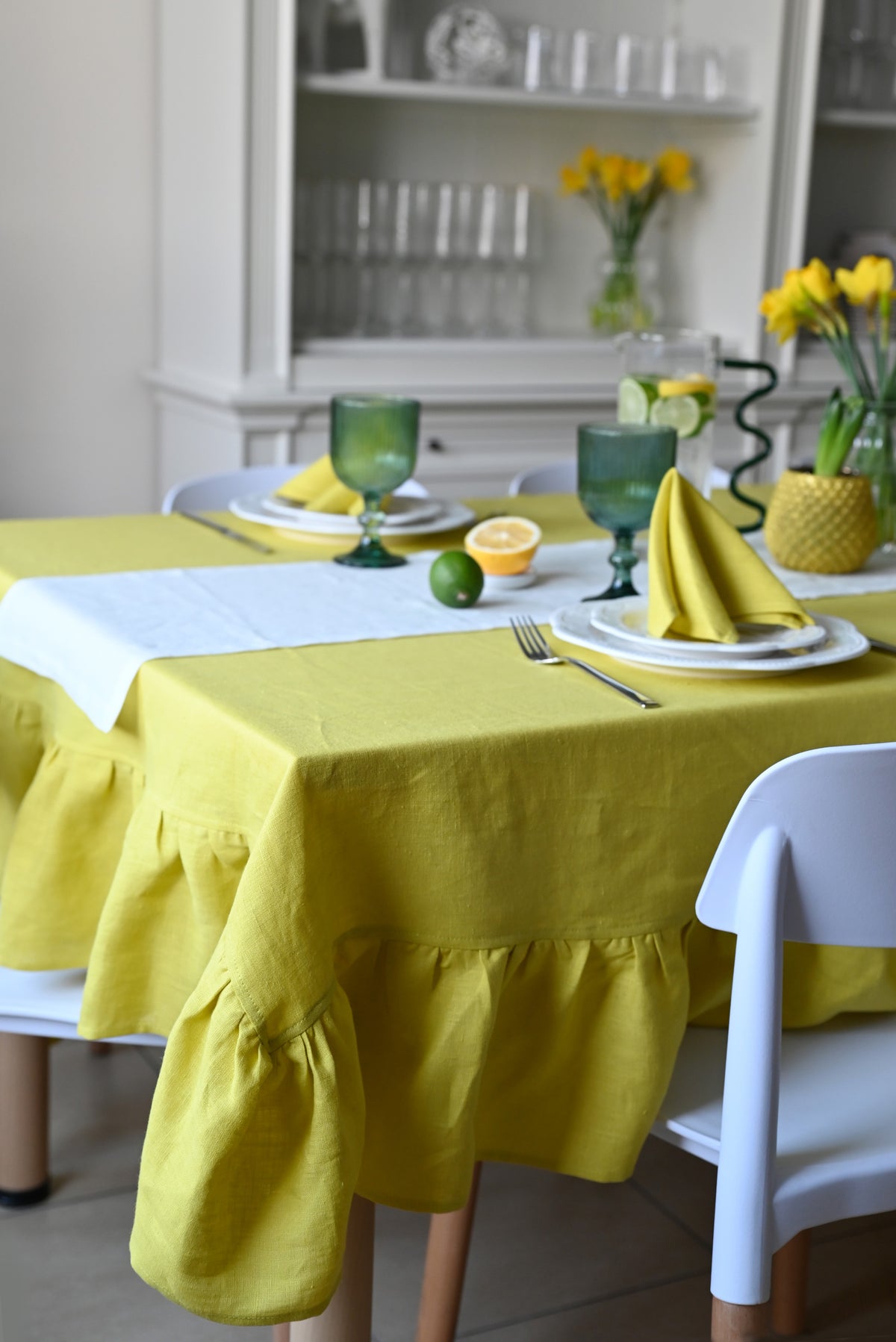Dining table set with a chartreuse tablecloth, plates, and cutlery in a kitchen.