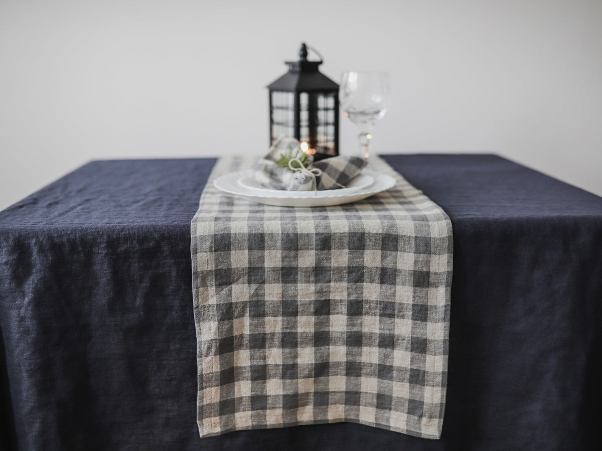 Table setting with a checkered runner, candle, and glass on a dark gray tablecloth.