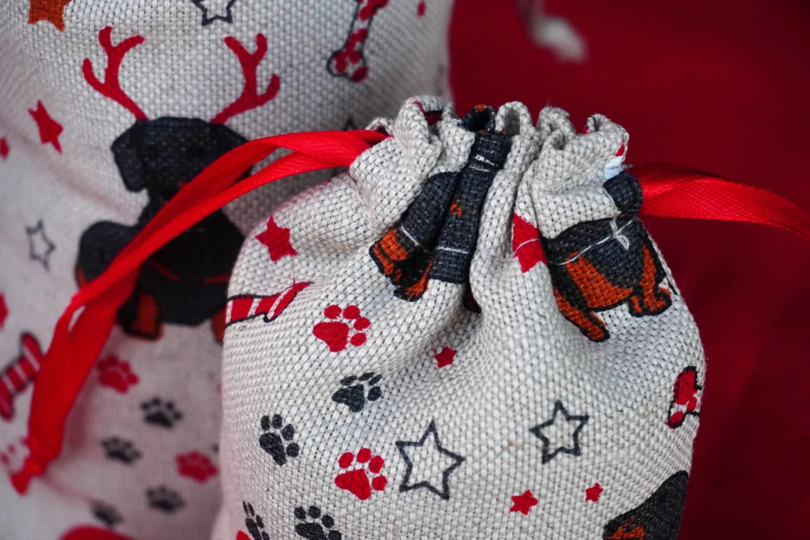 A close-up of a small fabric drawstring bag with a red ribbon, printed with black and red dog silhouettes