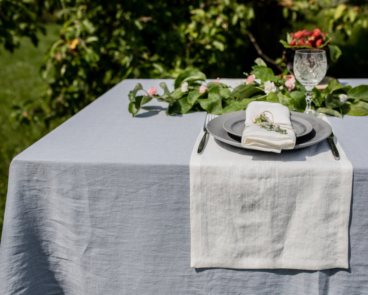 Elegant outdoor table setting with dusty blue tablecloth, floral decorations, and silverware.