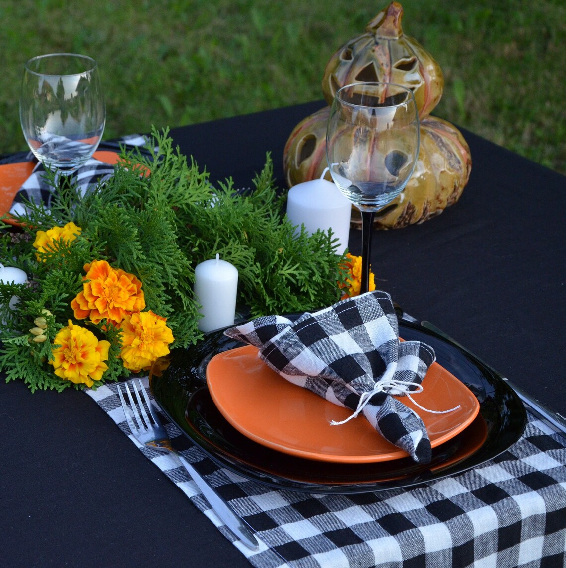 Halloween-themed table setting with orange plates, black  gingham linen napkins, and decorative pumpkins.