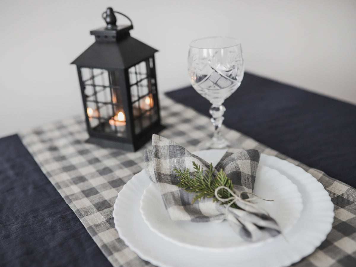 Table setting with a black lantern, glass, and checkered linen napkin on a checkered tablecloth.