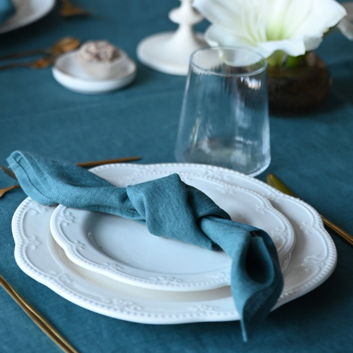 Elegant table setting with teal napkins, white plates, and a candle on a blue tablecloth.