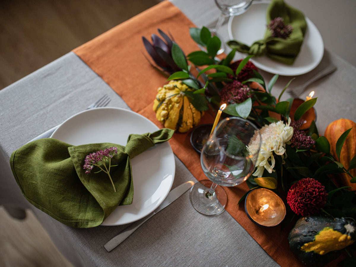 Decorative table setting with olive green napkins, candles, and pumpkins on a gray tablecloth.