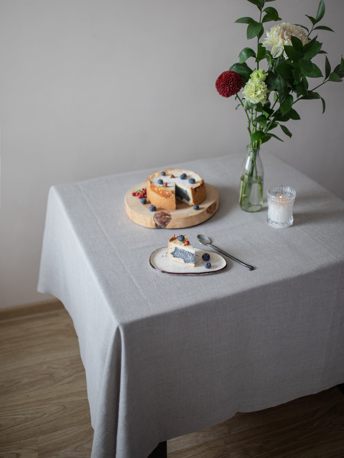 Table setting with a cake, flowers, and a candle on a natural linen tablecloth.