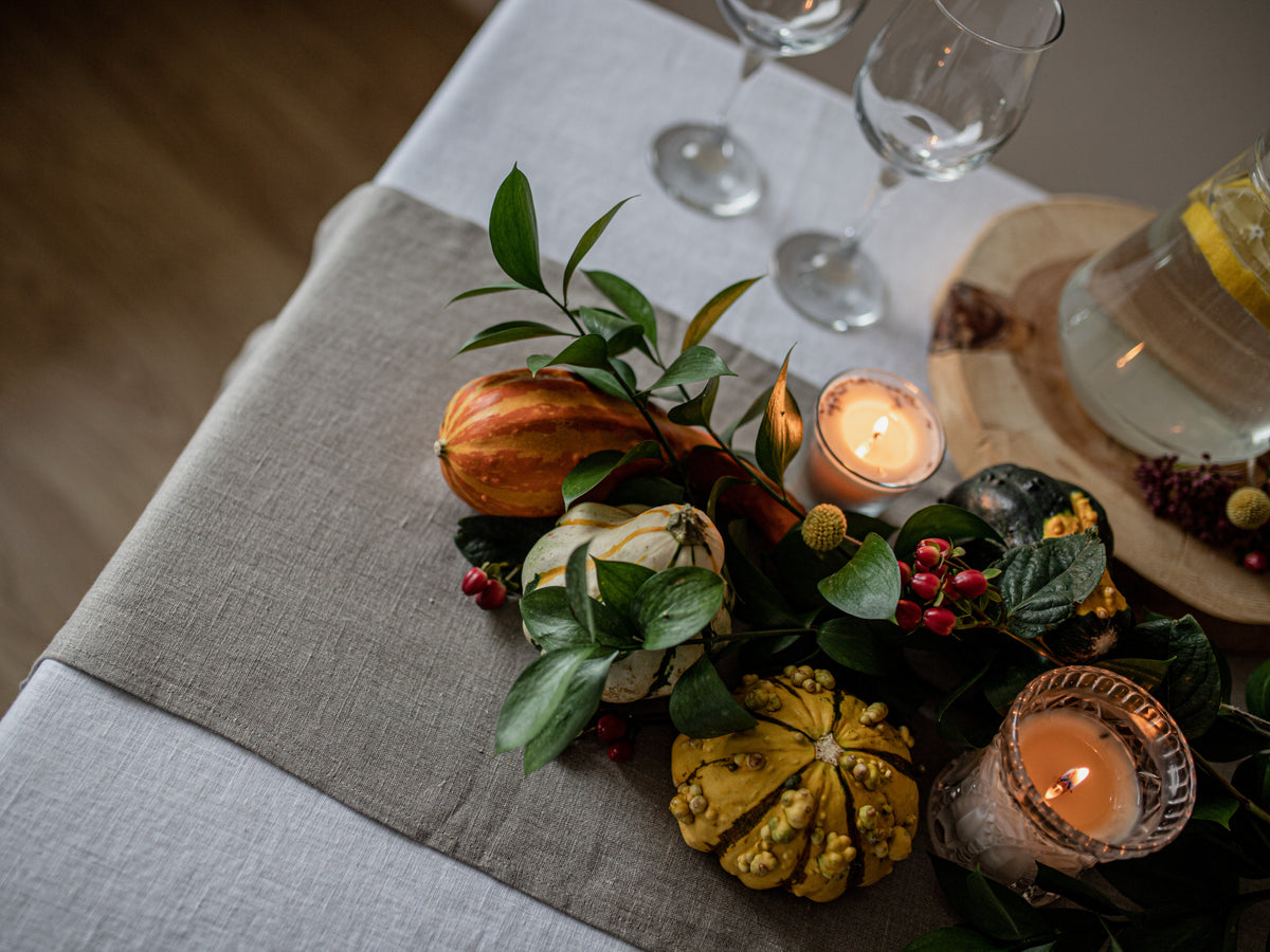 Decorative table setting with pumpkins, candles, and greenery on a tablecloth.