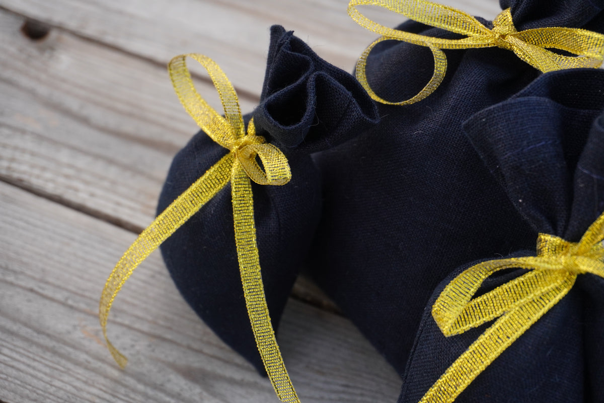 A close-up of dark navy blue  linen fabric bags tied with shiny yellow ribbon, placed on a weathered wooden surface.