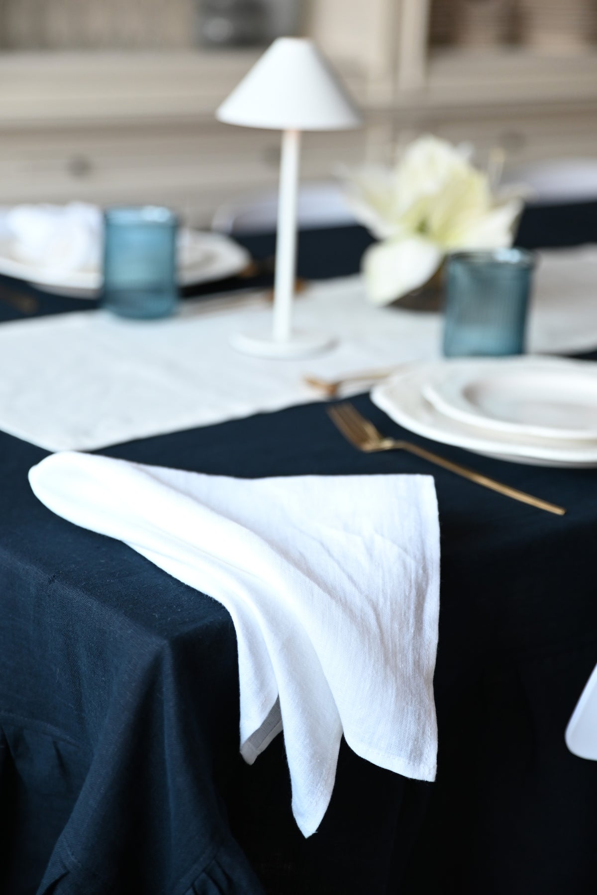 Navy linen tablecloth with white napkin and silverware on a dining table.