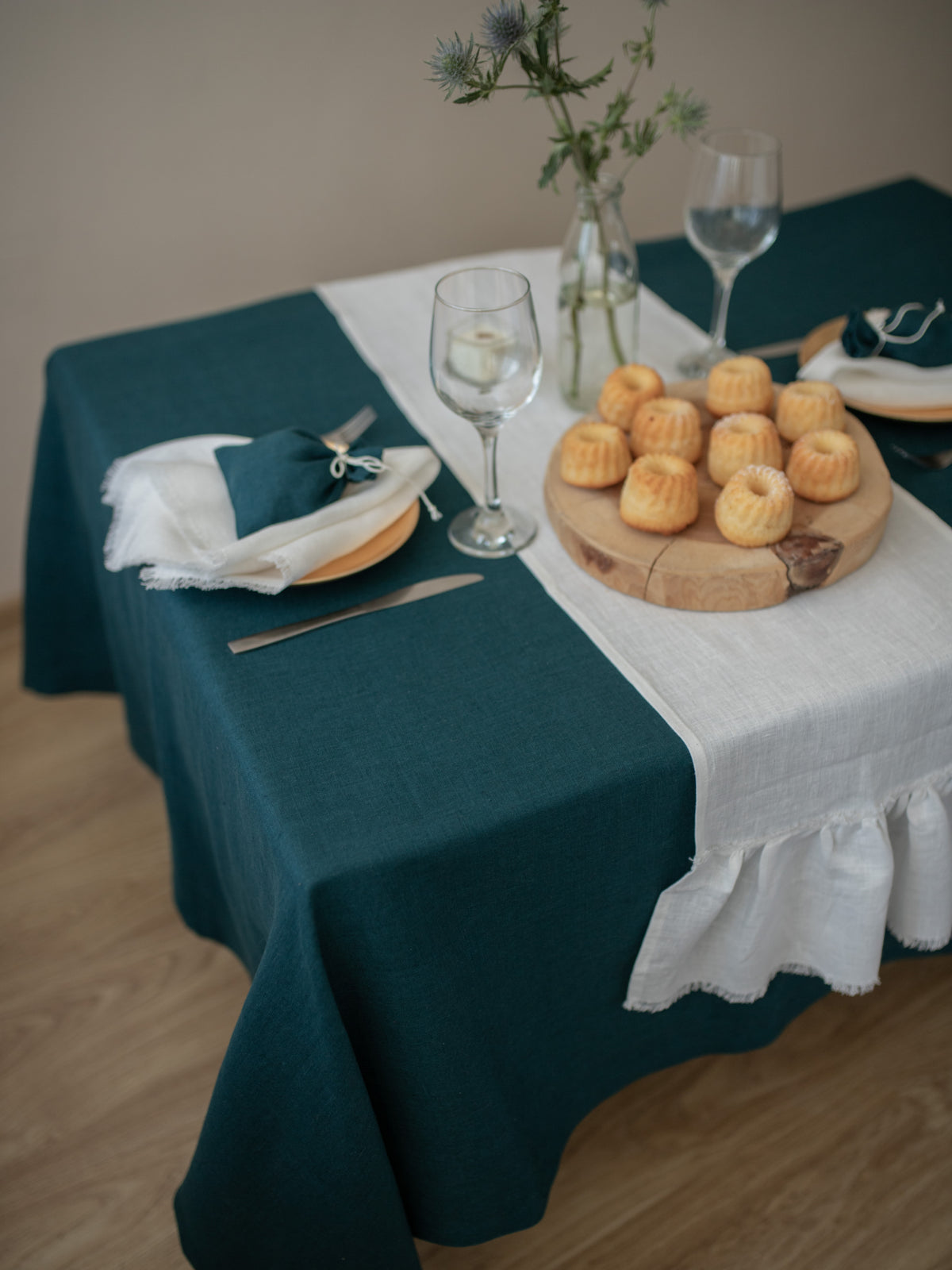 Set table with green tablecloth, white linen table runner and bread on a wooden floor.