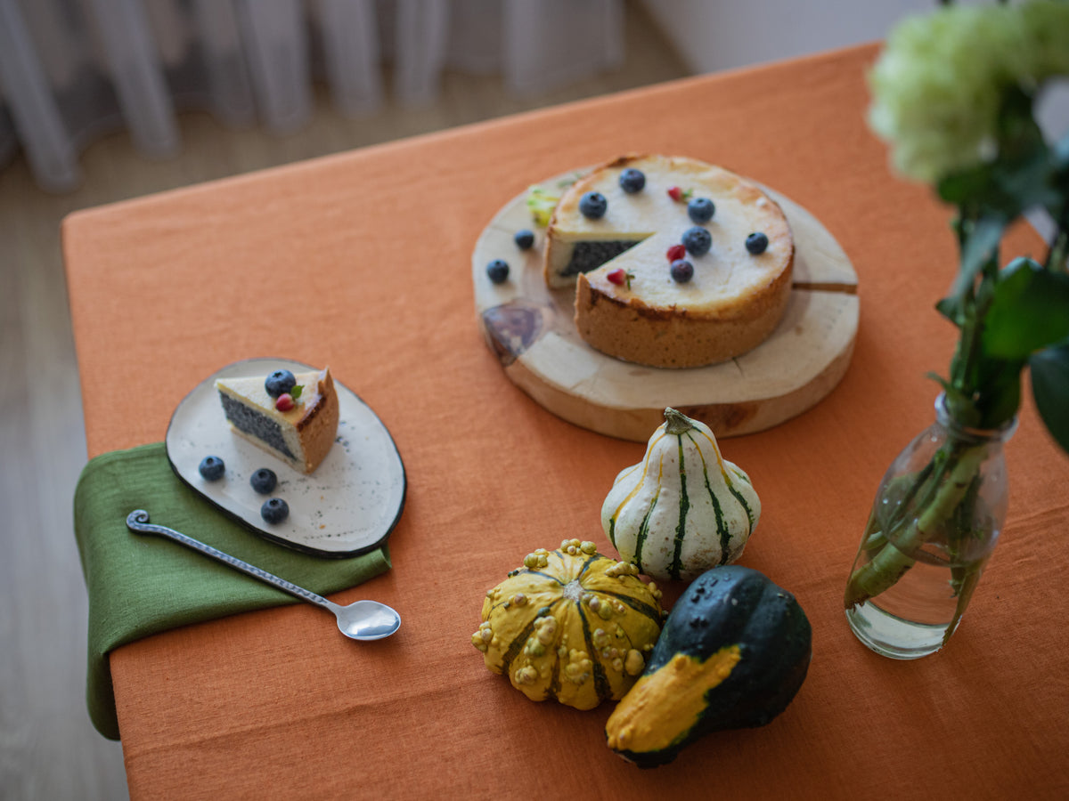 Small cake on a plate with a slice cut out, surrounded by decorative gourds and a vase of flowers on an orange tablecloth with olive green linen napkin.