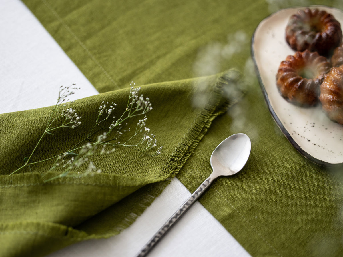 Olive Green Fringed  linen napkin with a spoon and fruits.