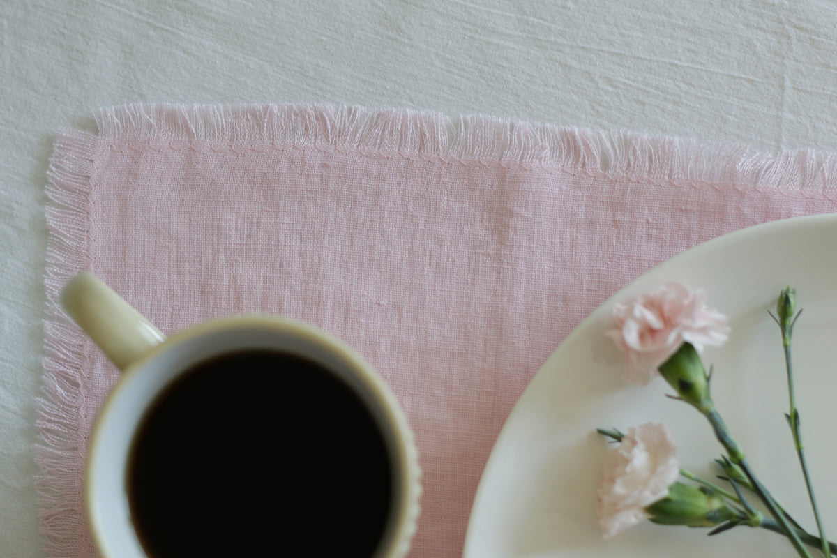 Cup of coffee on a pink linen  napkin with a plate of flowers