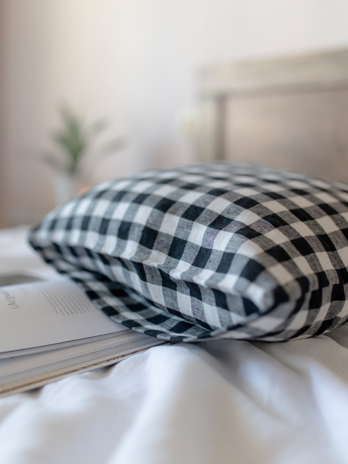 Black and white checkered linen pillow on a white surface with a blurred background