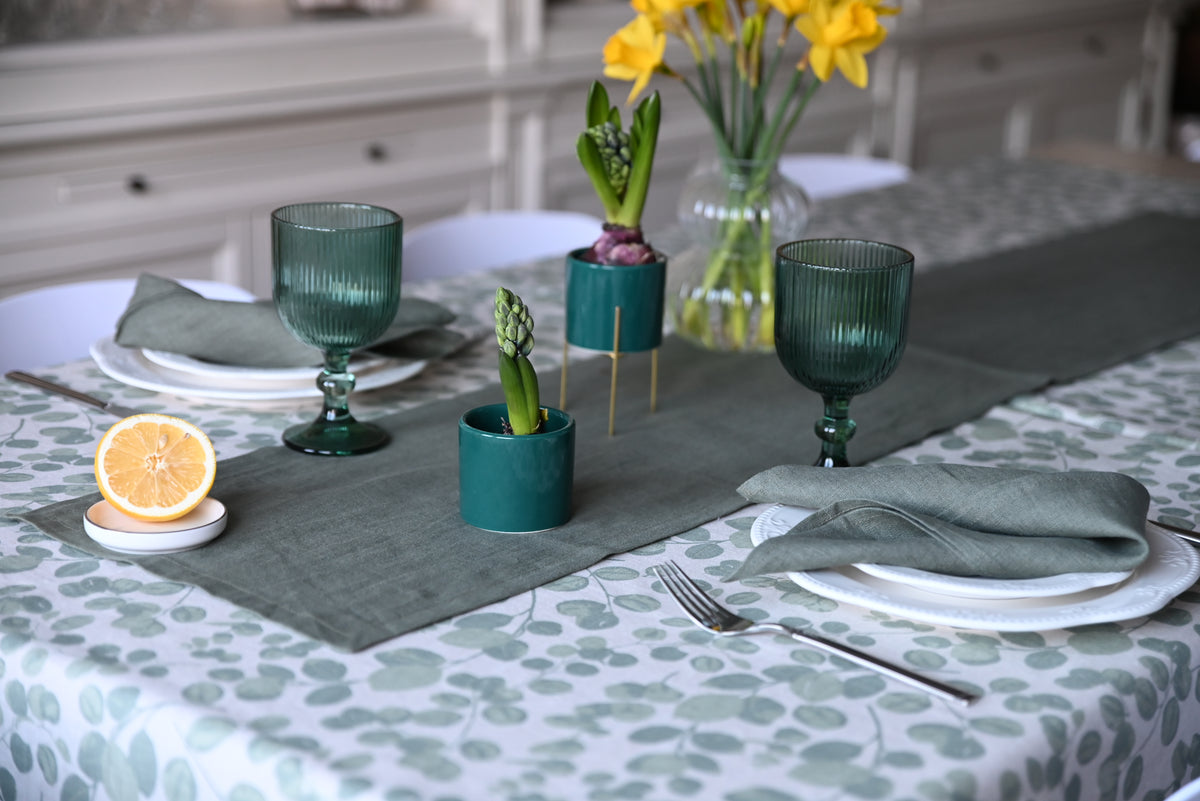 Table setting with green glasses, lemon, and flowers on a patterned linen  tablecloth.