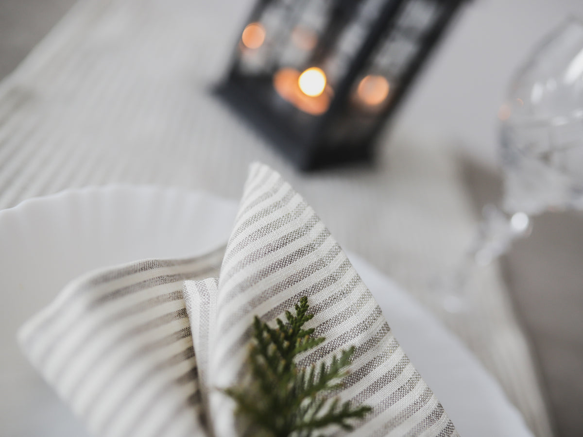 Striped napkin with a green leaf on a white surface with a blurred candle in the background