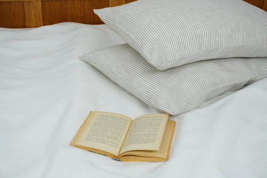 Open book on a bed with white sheets and striped pillows