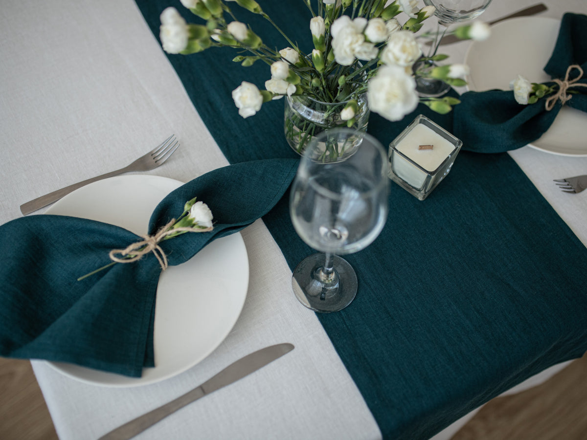 Elegant table setting with teal linen napkins, white flowers, and clear glasses on a white tablecloth.