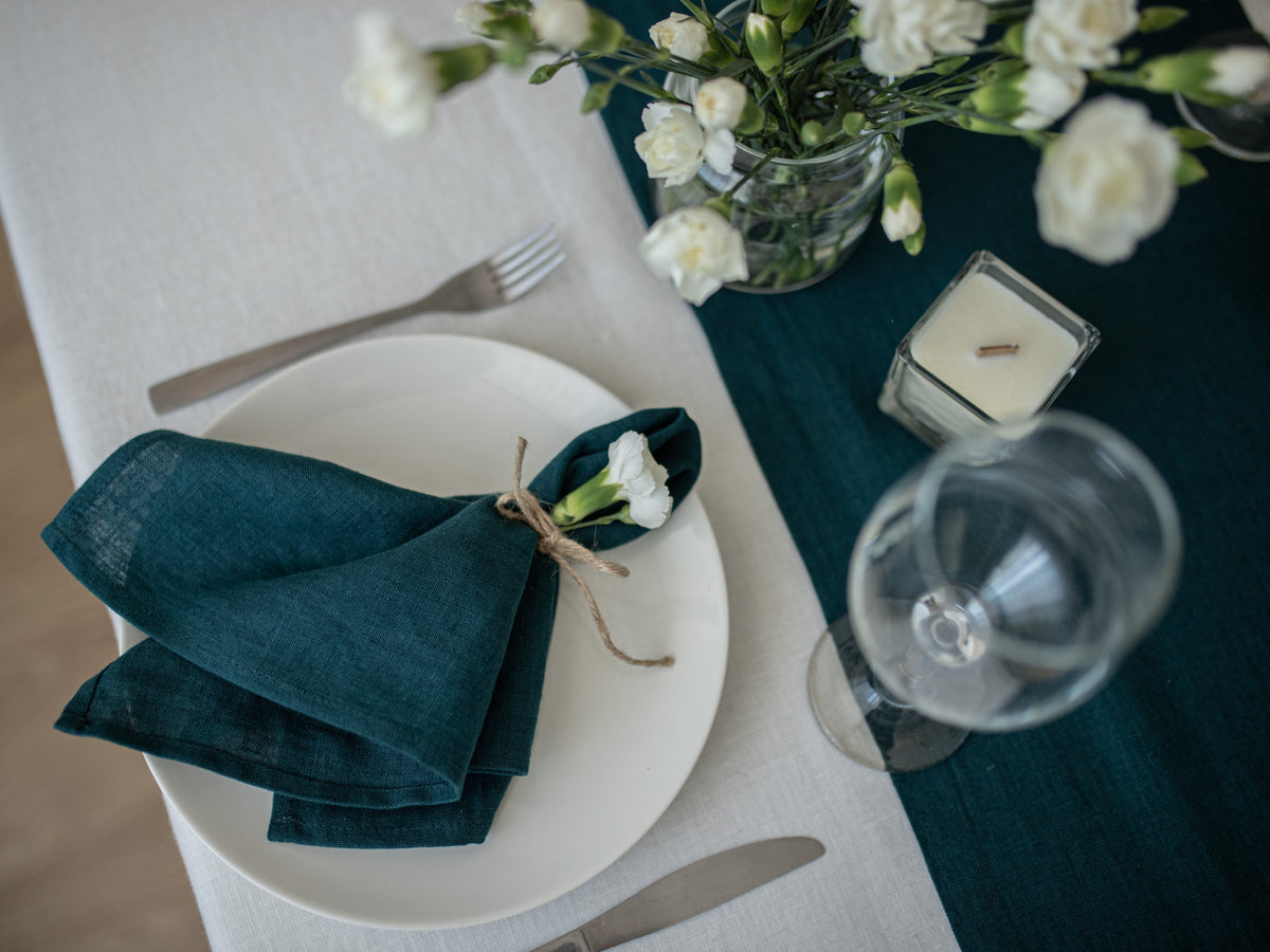Dining table setting with white plate, emerald green napkin, and floral arrangement.