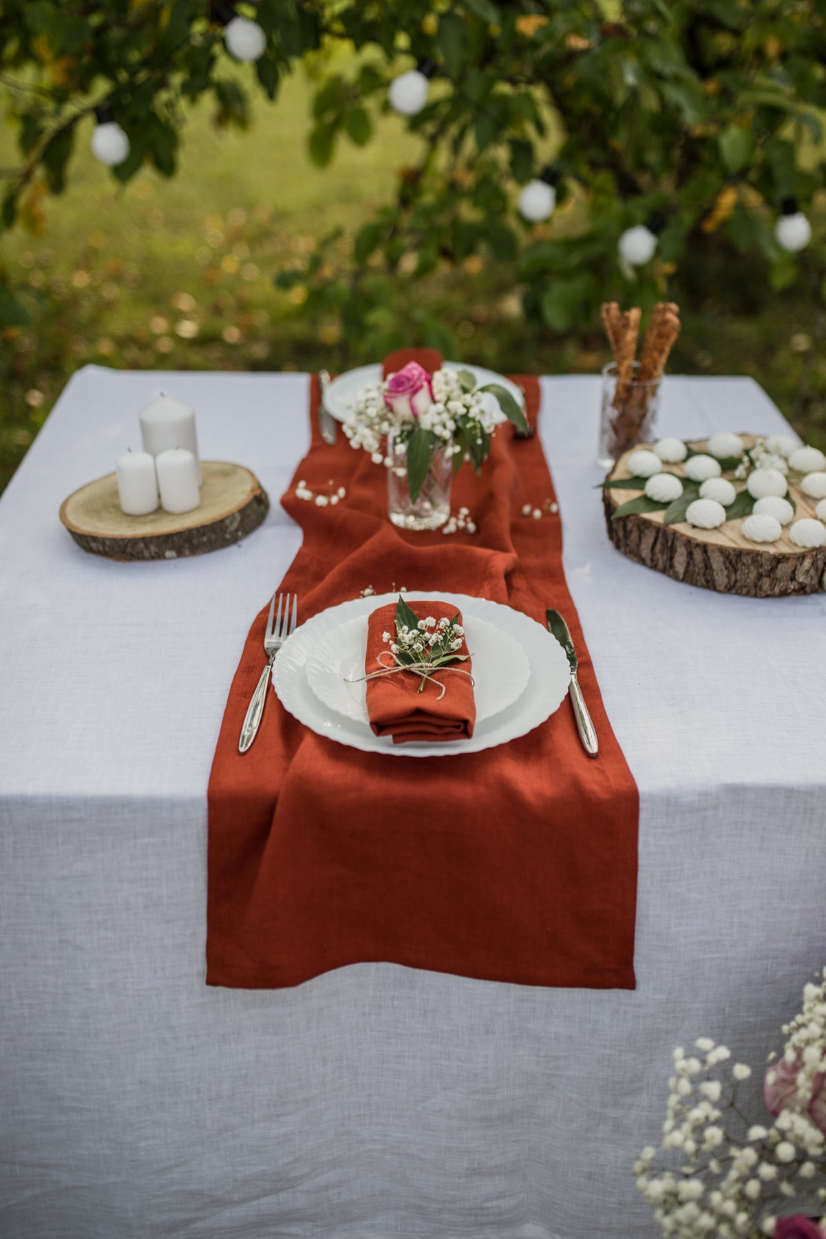 Table setting with terracotta napkins, white plates, and floral decorations outdoors.