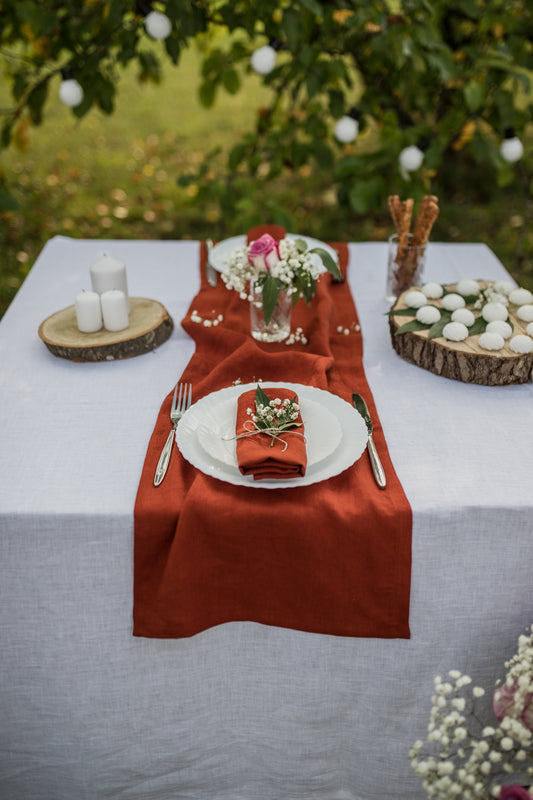 Table setting with terracotta napkins, white plates, and floral decorations outdoors.