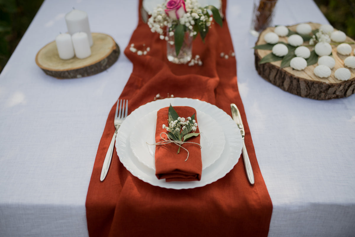 Decorative table setting with terracotta napkin, white plate, and floral arrangement on a white tablecloth.