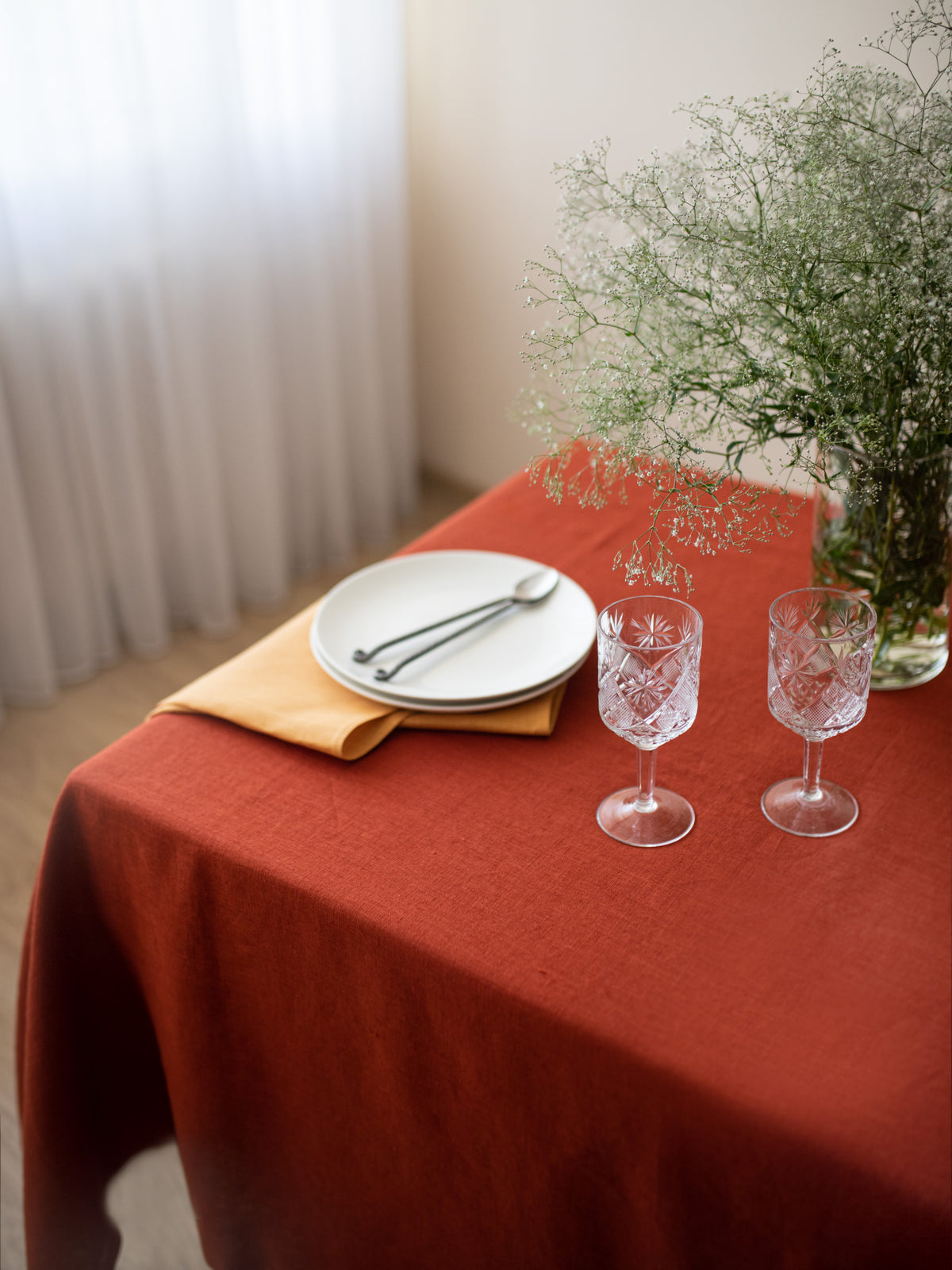 Burnt orange linen tablecloth styled with tableware, glasses and linen napkins