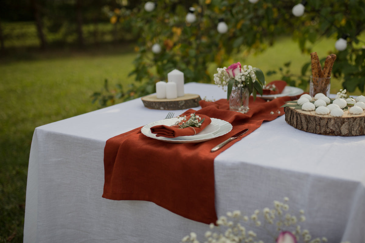 Decorated outdoor table with white tablecloth, natural linen terracotta tablerunner