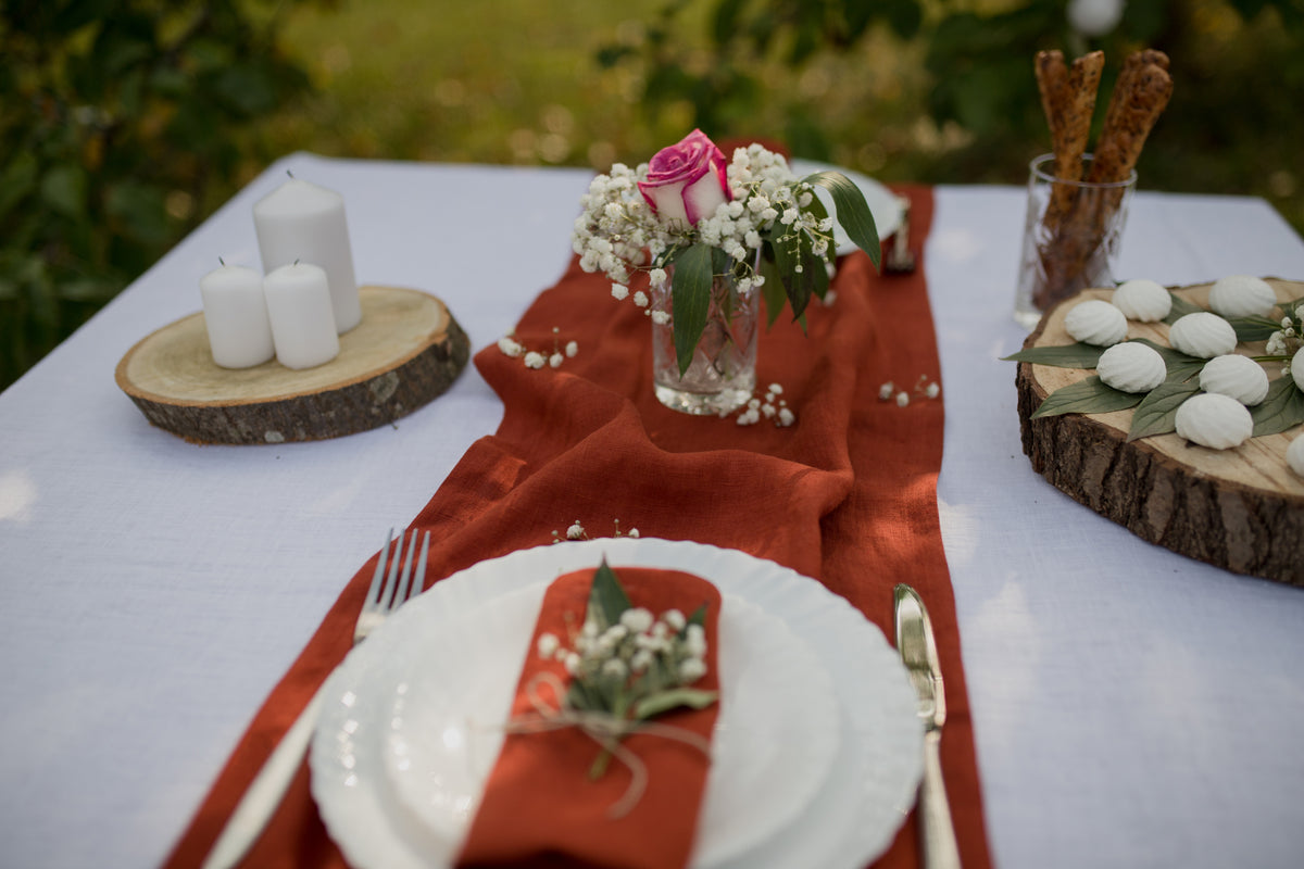 Decorative table setting with candles, flowers, and cutlery on a white tablecloth with terracota linen napkin