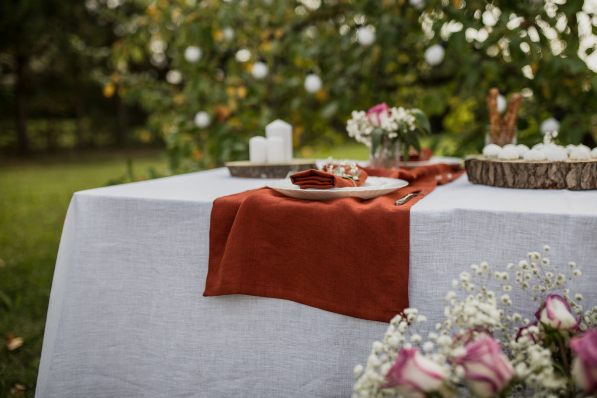 Wedding Table setting with a terracotta handmade table runner and white tablecloth outdoors