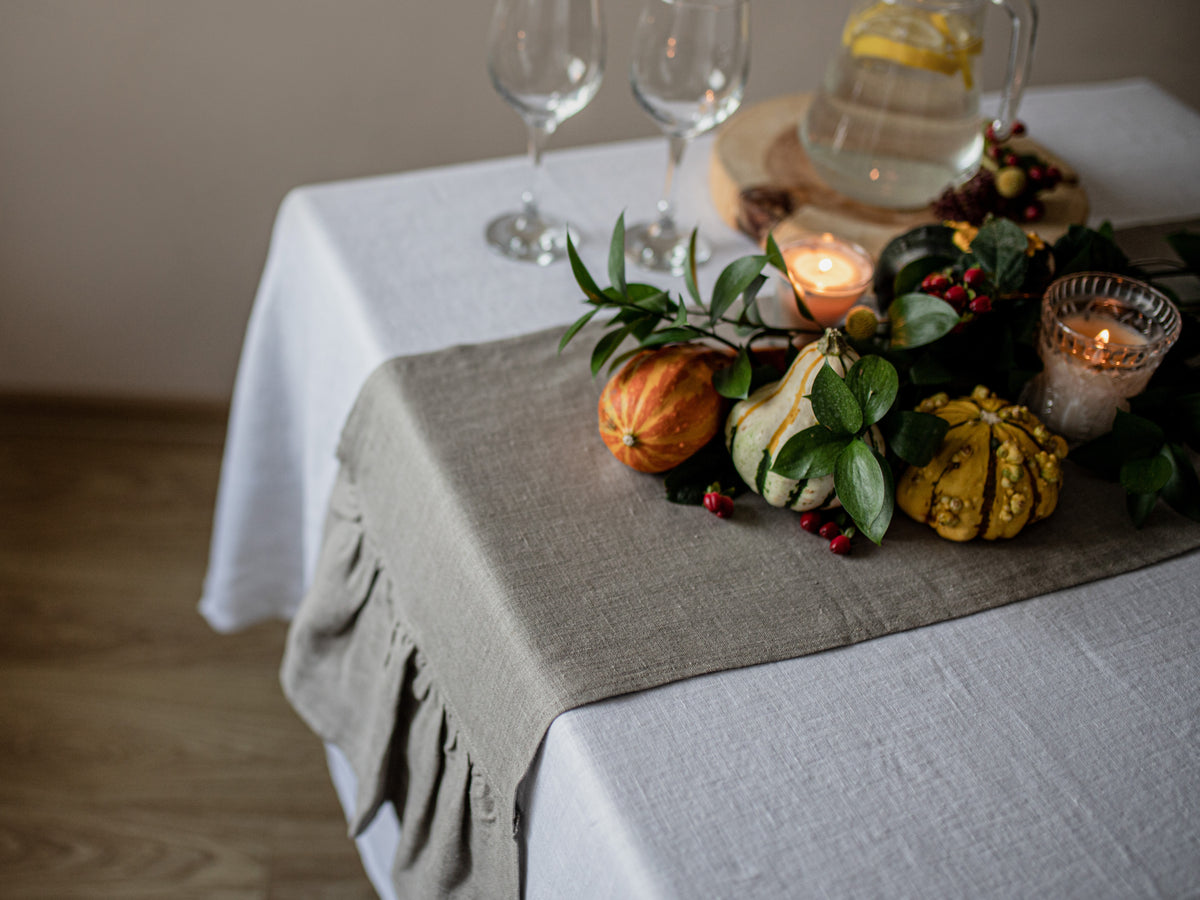 Decorative table setting with pumpkins, candles, and glasses on a white tablecloth.