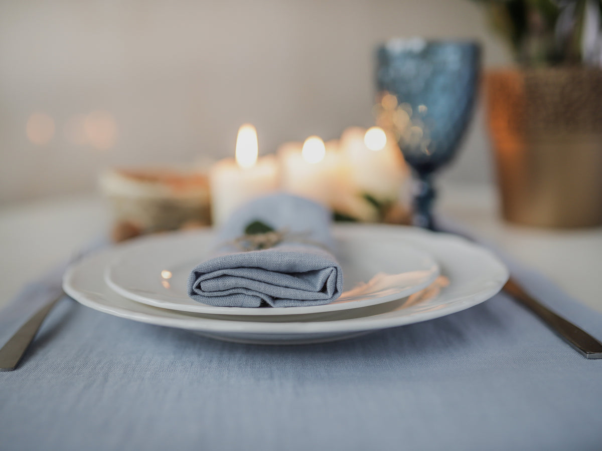 Dinner setting with candles, plates, and a dusty blue napkin on a table.